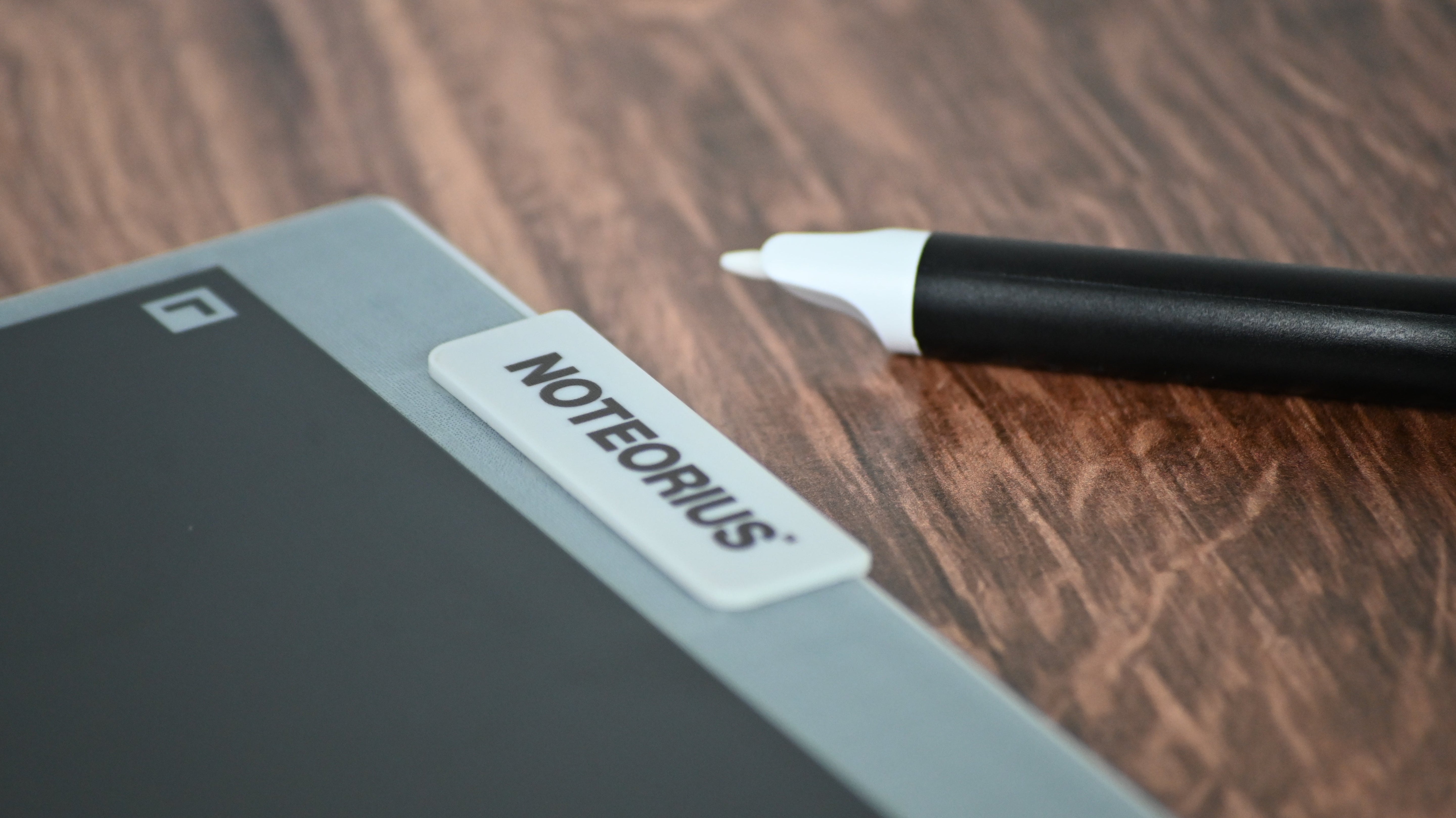 Digital display with stylus on a wooden surface, featuring the 'Noteorius' smart notebook.