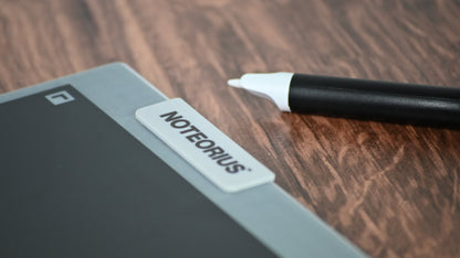 Digital display with stylus on a wooden surface, featuring the 'Noteorius' smart notebook.